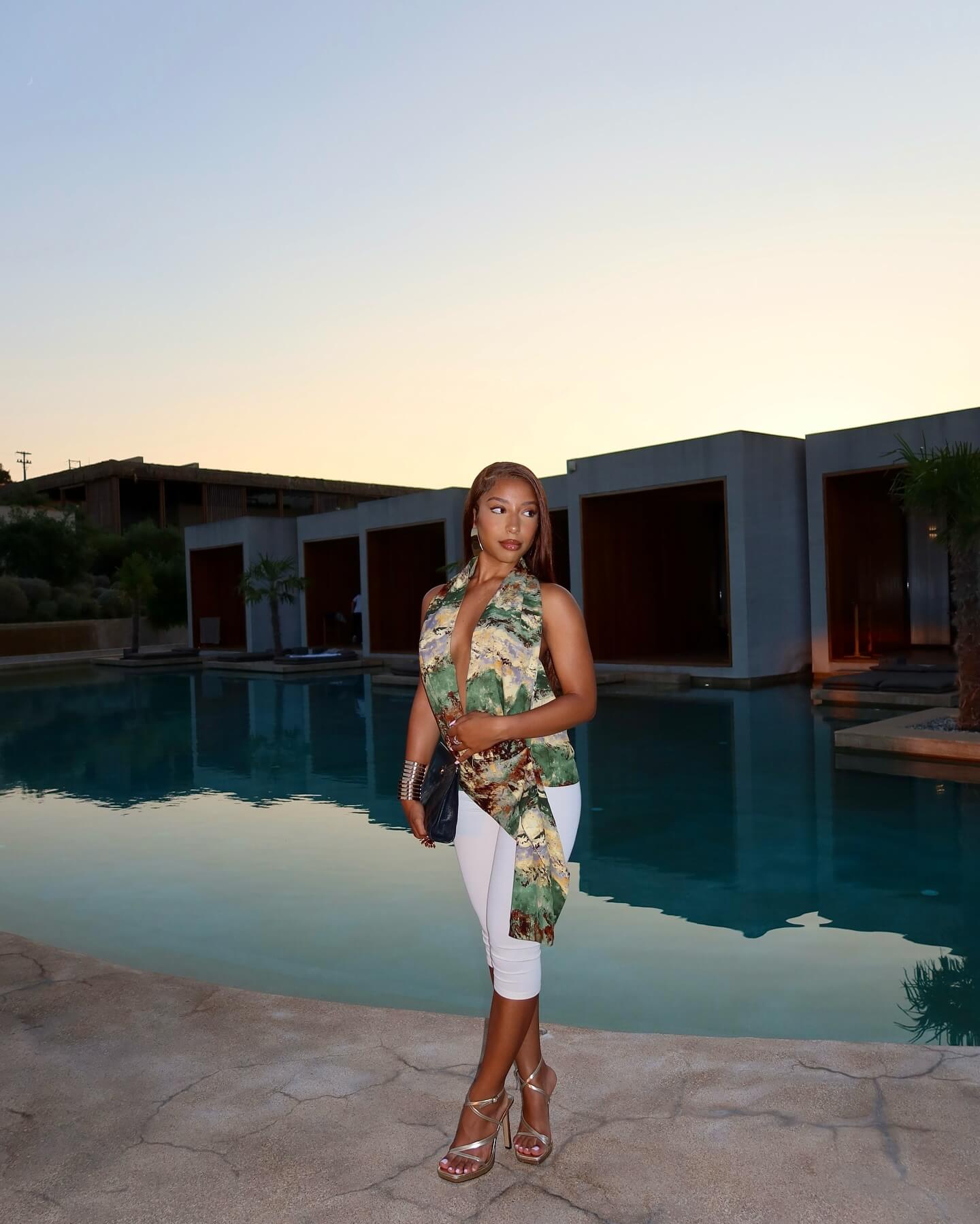 A woman wearing light linen trousers and a white mini tee, stood in front of plants