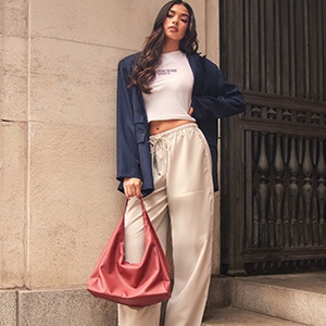 A woman leaning up a wall, with a blue blazer and khaki chino trousers